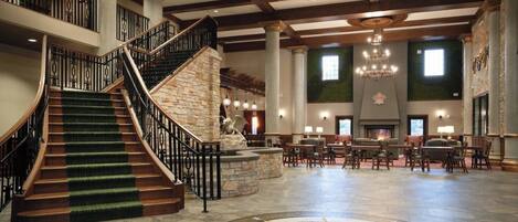 A spacious lobby with a grand staircase, a stone fireplace, and a large chandelier.