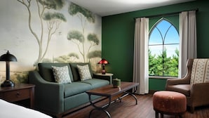 A room with a green wall, a large window with curtains, a sofa, a table, and a chair. - Dellshire Resort (Wisconsin Dells)