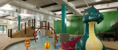 An indoor swimming pool with a large dinosaur sculpture, slides, and a netted climbing area.