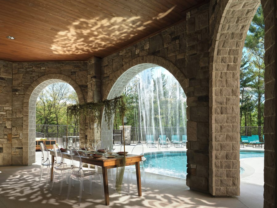 A stone archway leading to a pool area with clear chairs and a dining table set for two.