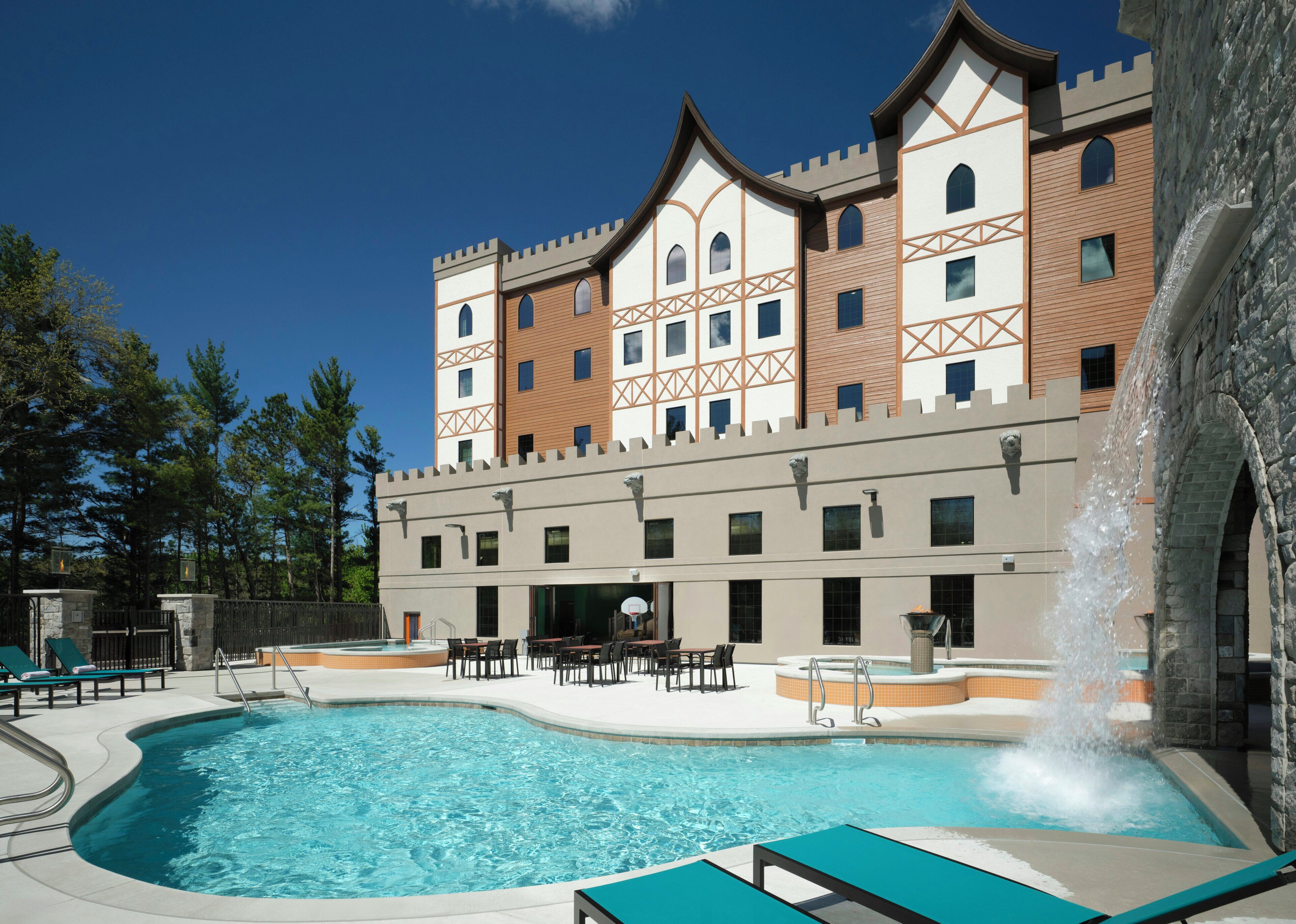 A hotel with a swimming pool, outdoor seating, and a castle-like facade.