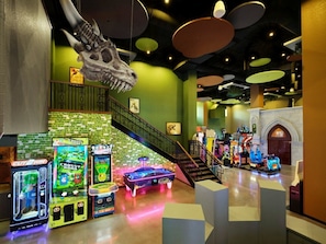 Une salle d’arcade avec différents jeux, un escalier et un crâne de dinosaure servant de décoration.