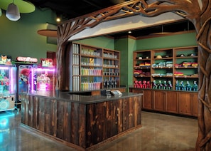 Un mostrador de recepción de madera con estantes llenos de objetos coloridos, máquinas de videojuegos y una estructura que recuerda a un árbol.
