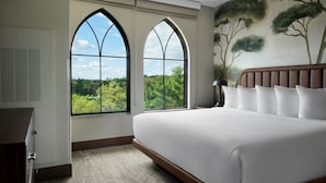 A bedroom with a large bed, two arched windows, a view of greenery, and a painting of trees on the wall. - Dellshire Resort (Wisconsin Dells)