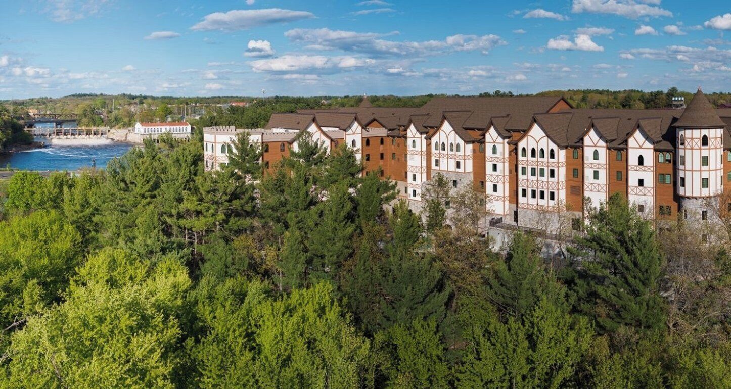 A row of traditional European-style buildings with a river and greenery in the foreground.