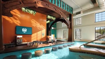 An indoor swimming pool with a wooden archway, a bar area, and a view of a waterfall.