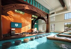 Una piscina interior con un arco de madera, una zona de bar y vistas a una cascada.