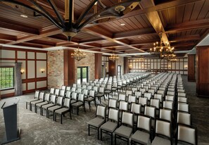 A conference room with rows of chairs, wooden ceiling beams, stone walls, and chandeliers. - Dellshire Resort (Wisconsin Dells)