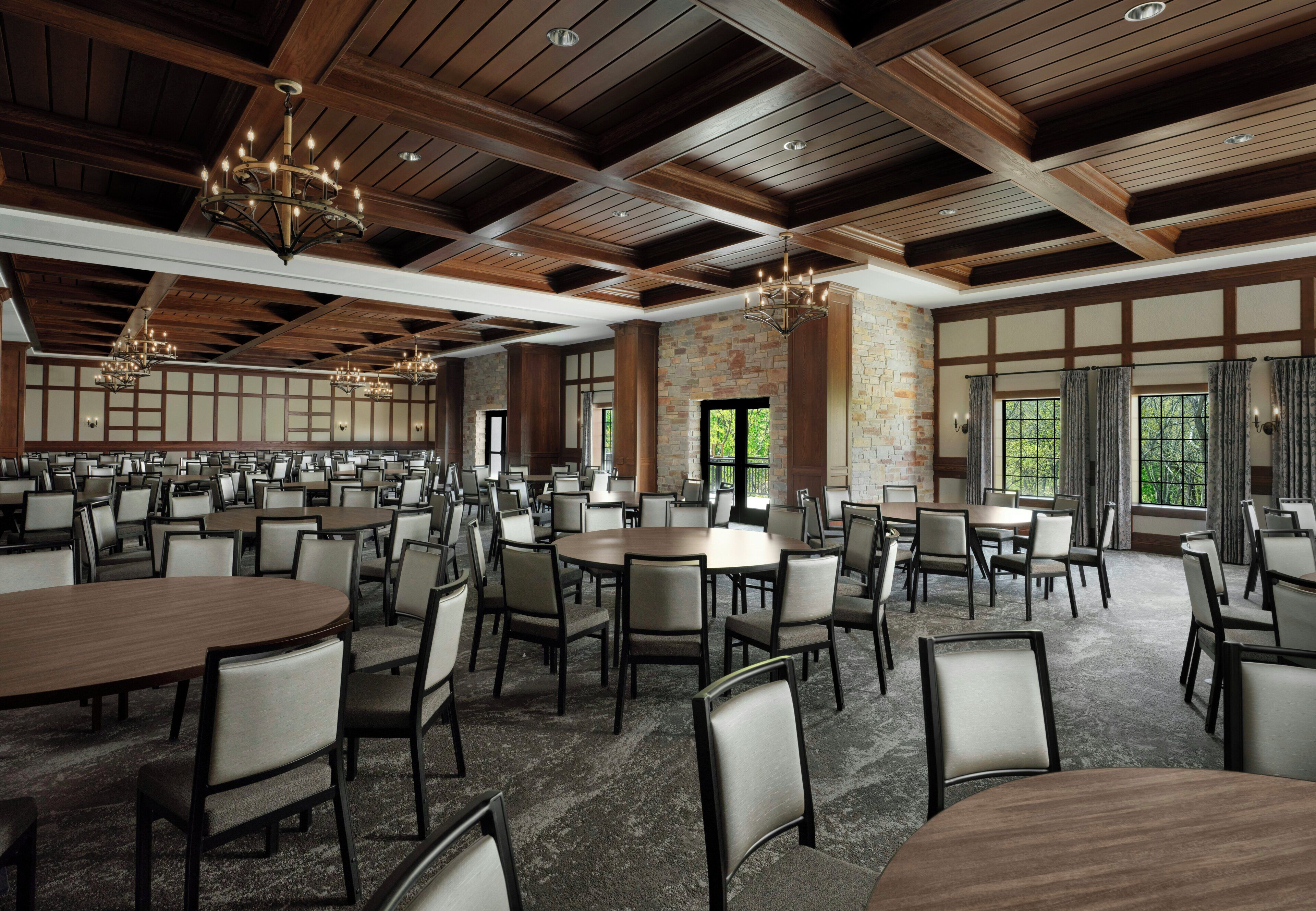A spacious conference room with multiple tables and chairs, wooden ceiling beams, and large windows.