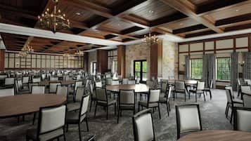 A spacious conference room with multiple tables and chairs, wooden ceiling beams, and large windows.