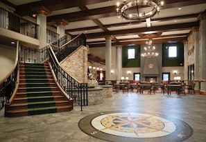 A spacious lobby with a grand staircase, a chandelier, and a stone fireplace. - Dellshire Resort (Wisconsin Dells)