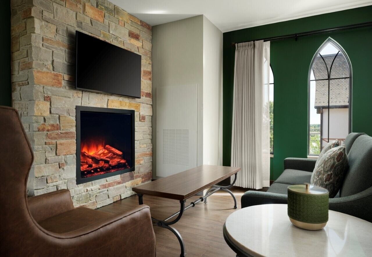 A room with a stone wall, a flat-screen TV, a fireplace, a table, and a green window.