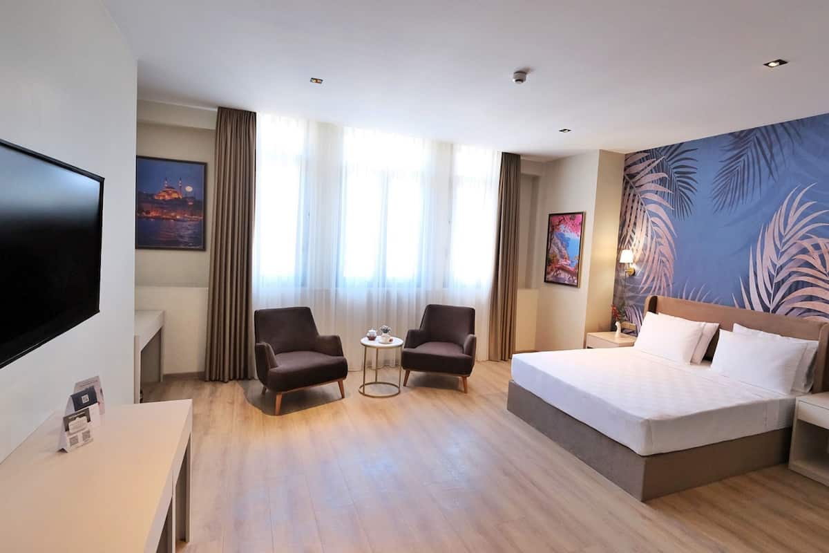 A hotel room with a large bed, two armchairs, a TV, and a desk.