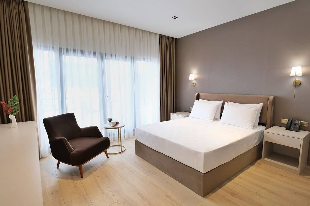 A hotel room with a large bed, a chair, a bedside table with a lamp, and a small table with a plant.