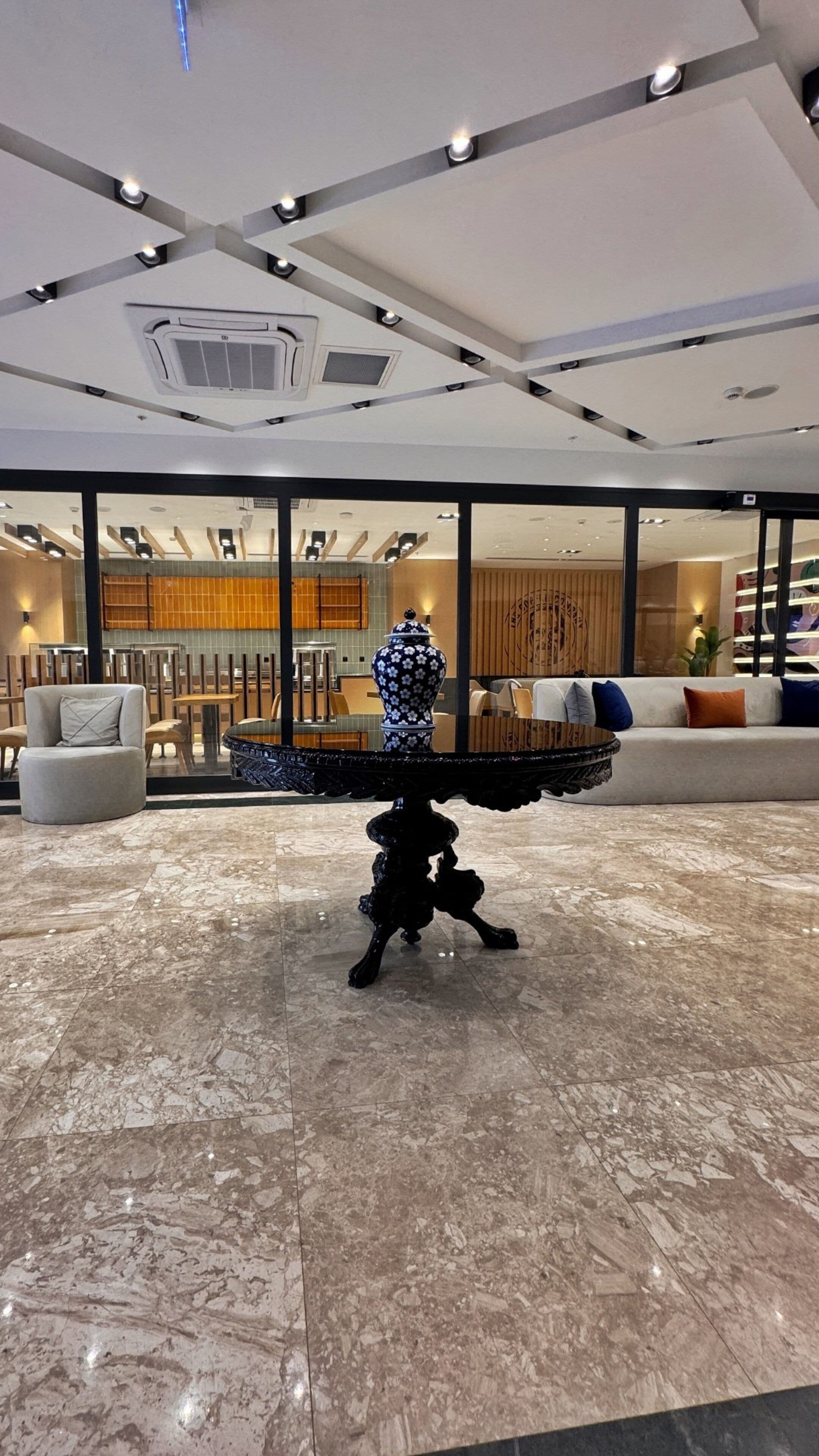 A modern lobby with a marble floor, a central black decorative piece, and seating areas with sofas and chairs.