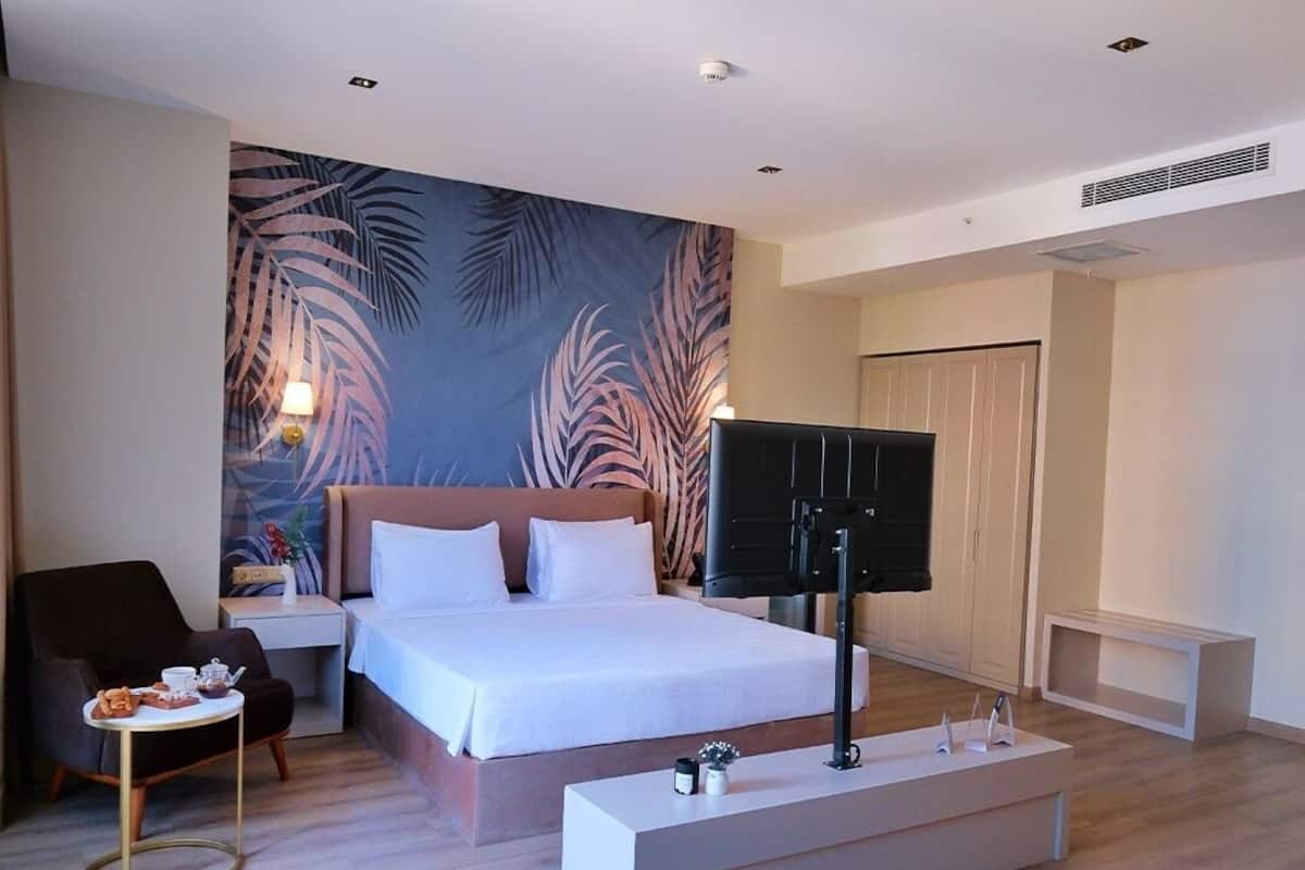 A modern hotel room with a large bed, a TV, a desk, and a sofa.