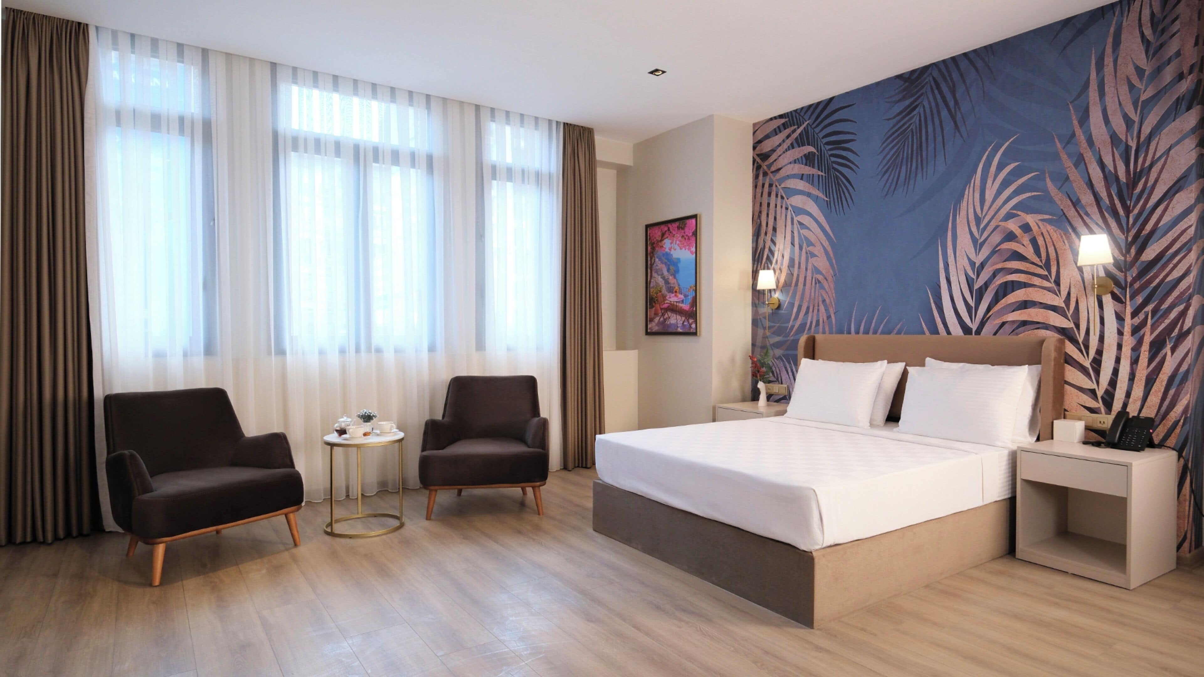 A hotel room with a large bed, two armchairs, a small table, and a painting on the wall.