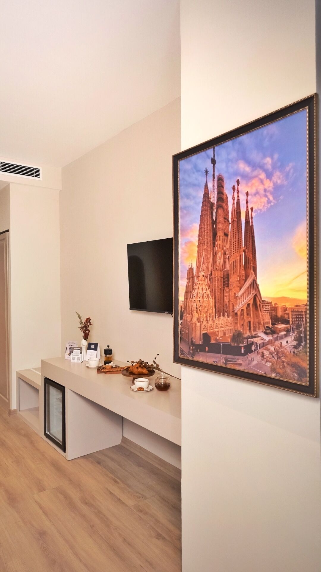 A modern living room with a flat-screen TV, a coffee table with a vase and a cup, and a framed picture of a cathedral on the wall.