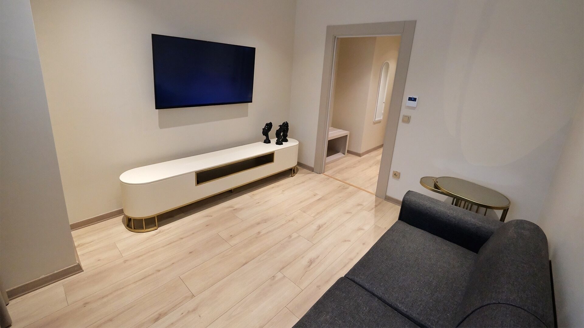 Un soggiorno moderno con un mobile TV bianco, un divano grigio e una TV a schermo piatto montata a parete.