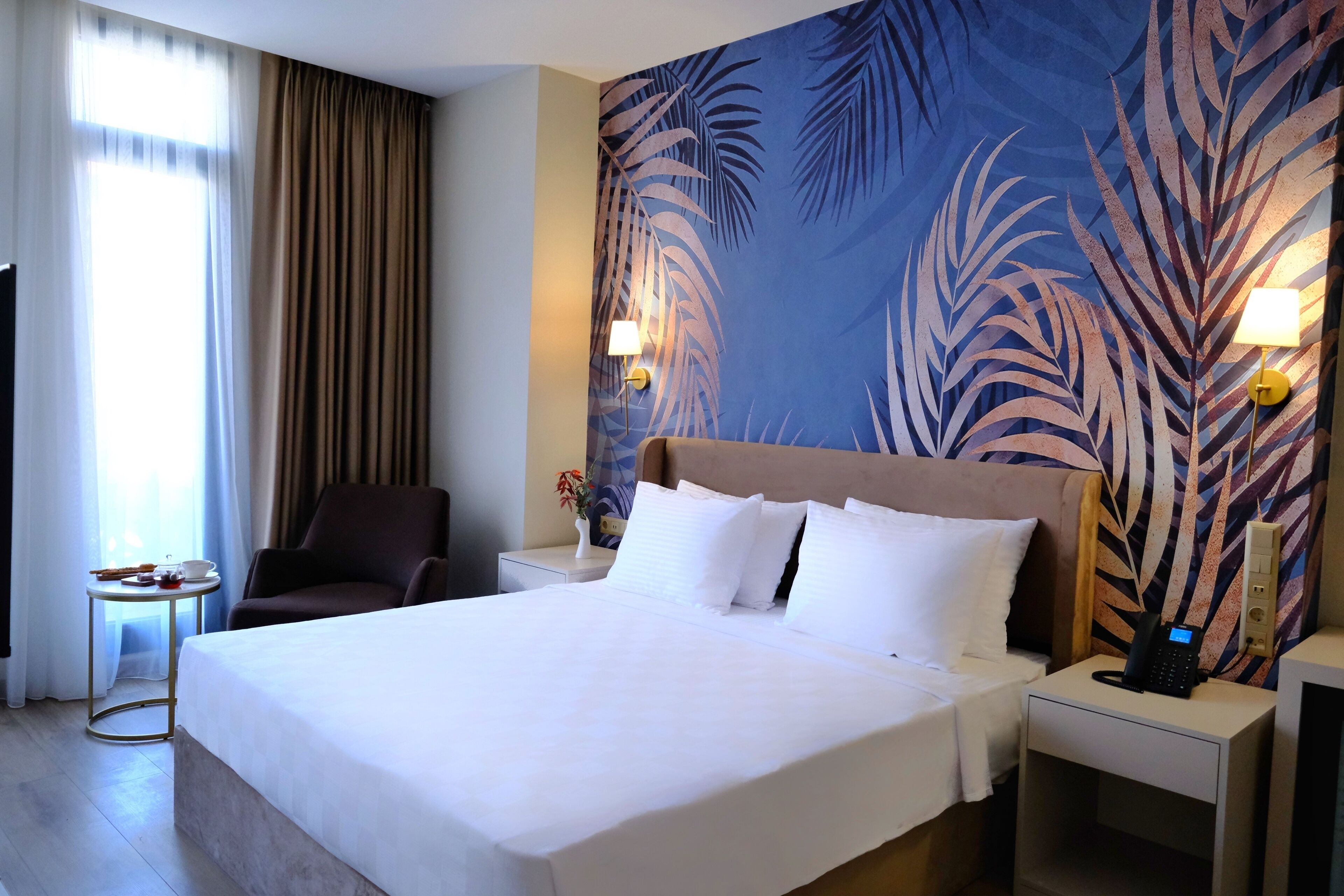 Une chambre d’hôtel avec un grand lit, une chaise, une petite table avec un vase et une table de chevet avec un téléphone.