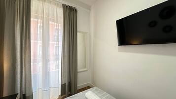 A room with a bed, a window with curtains, and a mounted television on the wall.