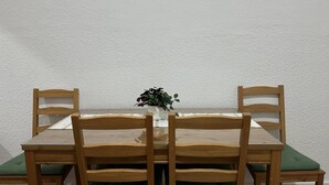 A dining table with four wooden chairs, a vase with a plant, and a green cushion on the seat of one chair. - Habitaciones Manuela (Madrid)