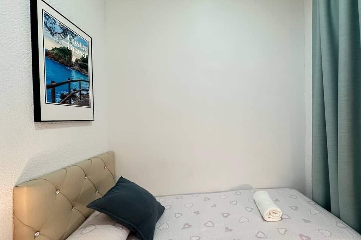 A bedroom with a bed, a headboard, a framed picture on the wall, and a window with curtains.