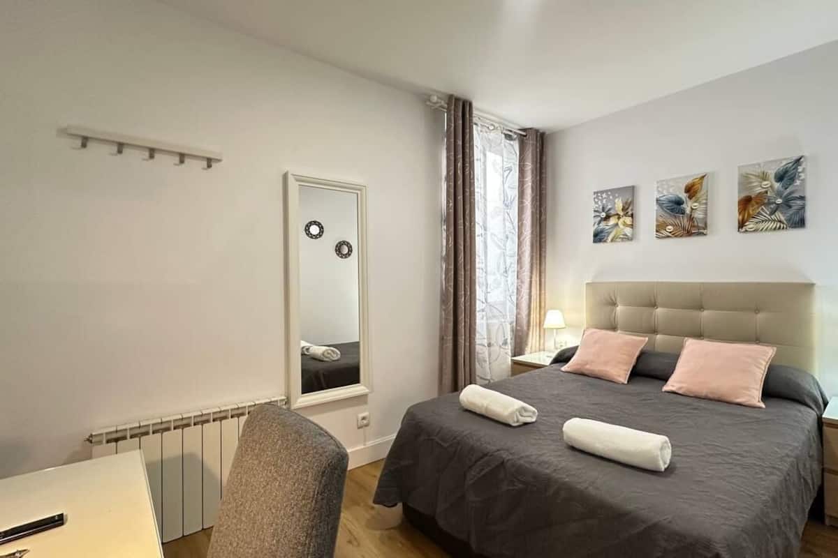 A bedroom with a bed, bedside tables, a mirror, and artwork on the wall.
