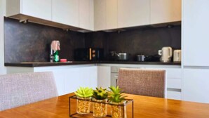Cocina moderna con armarios blancos, salpicadero oscuro y una mesa de comedor de madera con tres plantas en macetas.