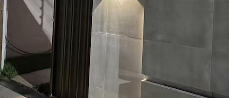 A modern building facade with a large, dark entrance door and a wall-mounted light fixture.