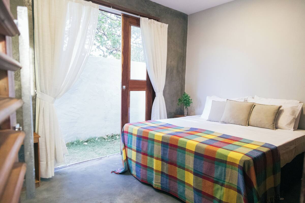 A bedroom with a bed, a window with curtains, and a small plant.