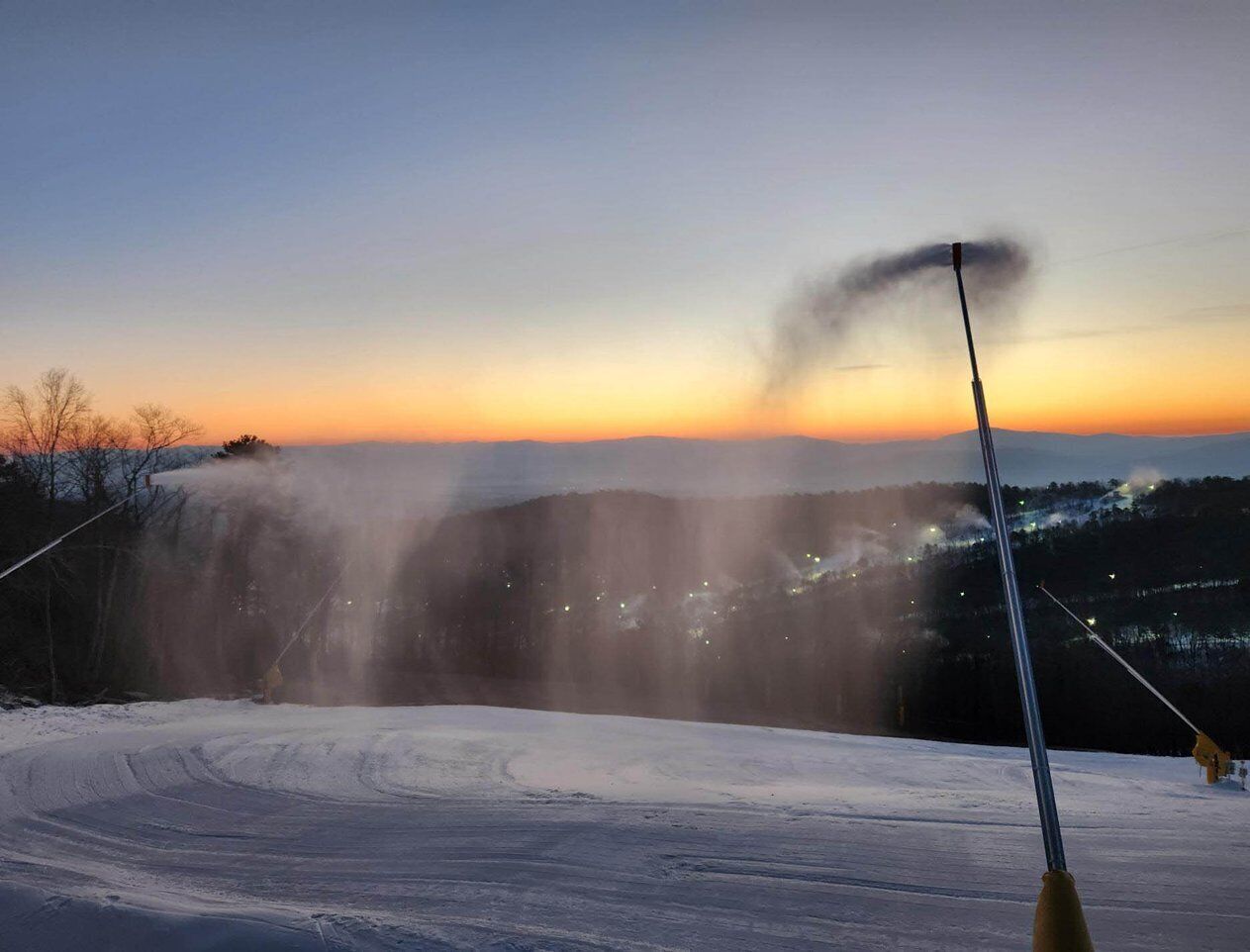 Schneebedeckte Landschaft mit Seilbahn und Sonnenuntergang im Hintergrund.