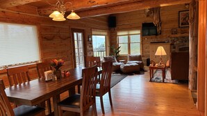 L’intérieur d’un chalet en bois comprend une table à manger, des chaises, un canapé, un téléviseur et une cheminée.