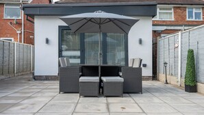 Eine Terrasse im Freien mit Tisch und Stühlen, einem großen Sonnenschirm und einem kleinen Topfpflanzen.