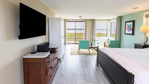 A hotel room with a bed, a TV mounted on the wall, a desk with a chair, and a view of the outdoors.