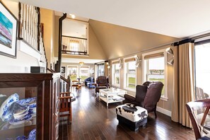 A spacious living area with a high ceiling, a staircase, and a view of the outdoors. - Elegant Waterfront Cottage – 3BR/3BA with Stunning River Views & Firepit (Stanley Bridge)
