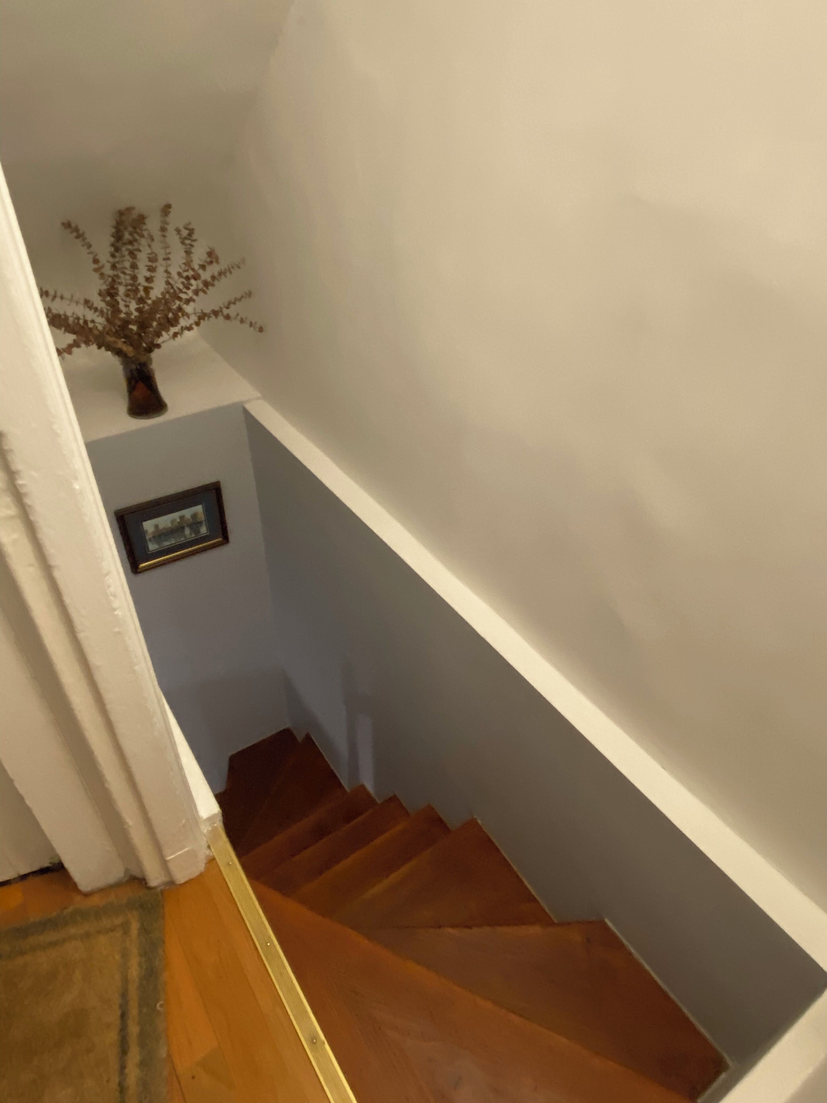 Una escalera de madera con una pared blanca y un cuadro enmarcado.