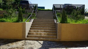 Eine Treppe führt im Freien zu einem Gebäude, umgeben von Grünpflanzen und Pflastersteinen.