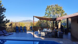 Ein Poolbereich mit überdachter Terrasse, Liegestühlen und Bergblick.