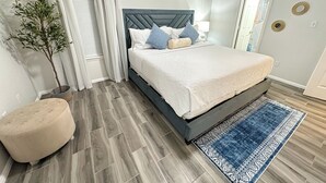 Un dormitorio con cama, mesita de noche, planta en maceta y alfombra azul.