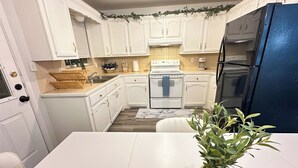 Una cocina compacta con armarios blancos, un refrigerador azul y una isla central con una planta.