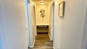 Un pasillo con piso de madera, una lámpara de pared y un letrero enmarcado.