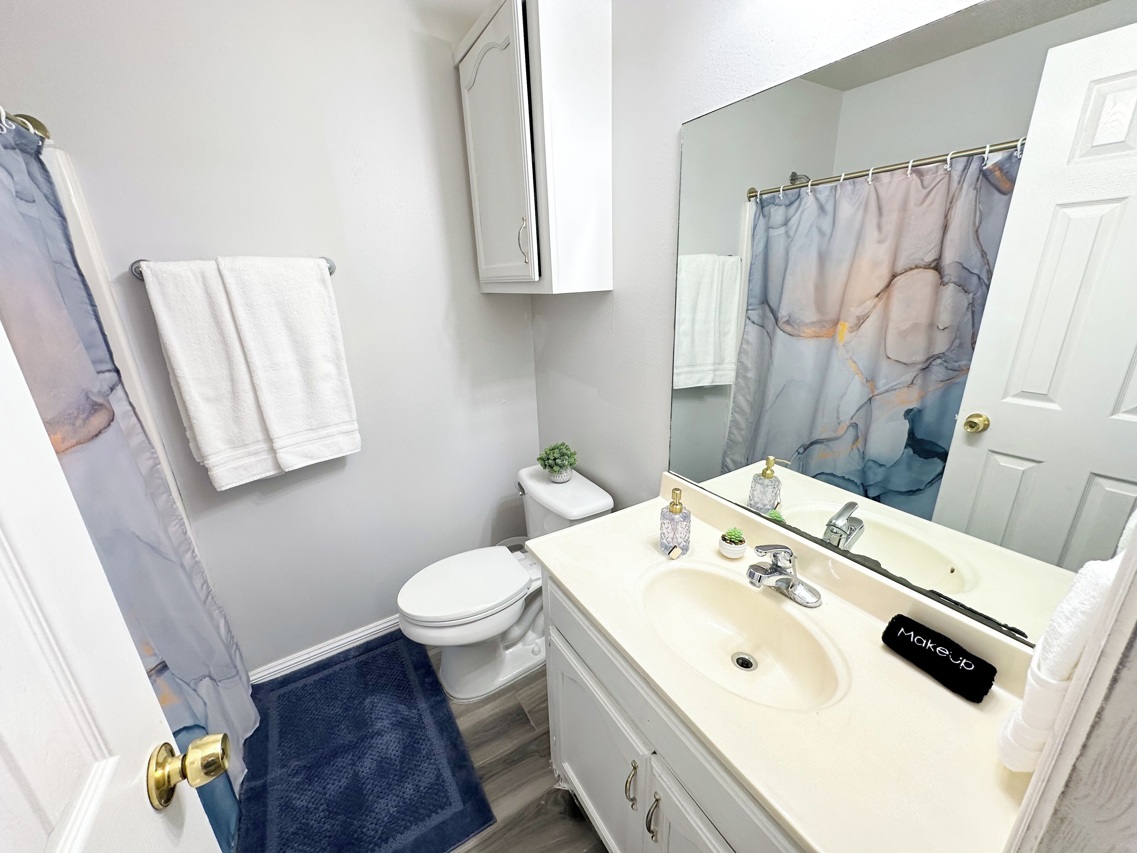 A bathroom with a toilet, sink, mirror, and a shower curtain.
