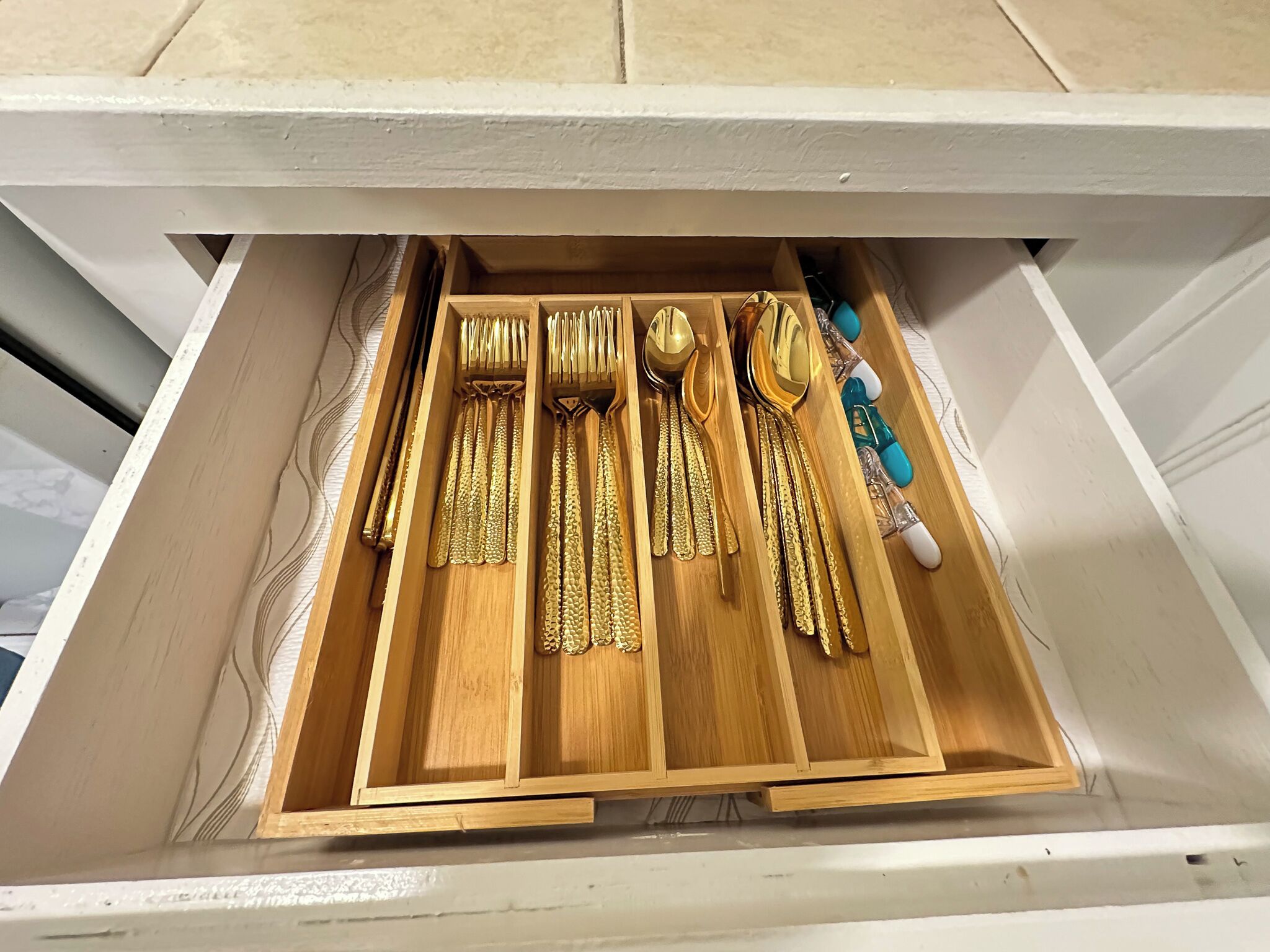 Un cajón con cubiertos dorados ordenados y una botella pequeña.