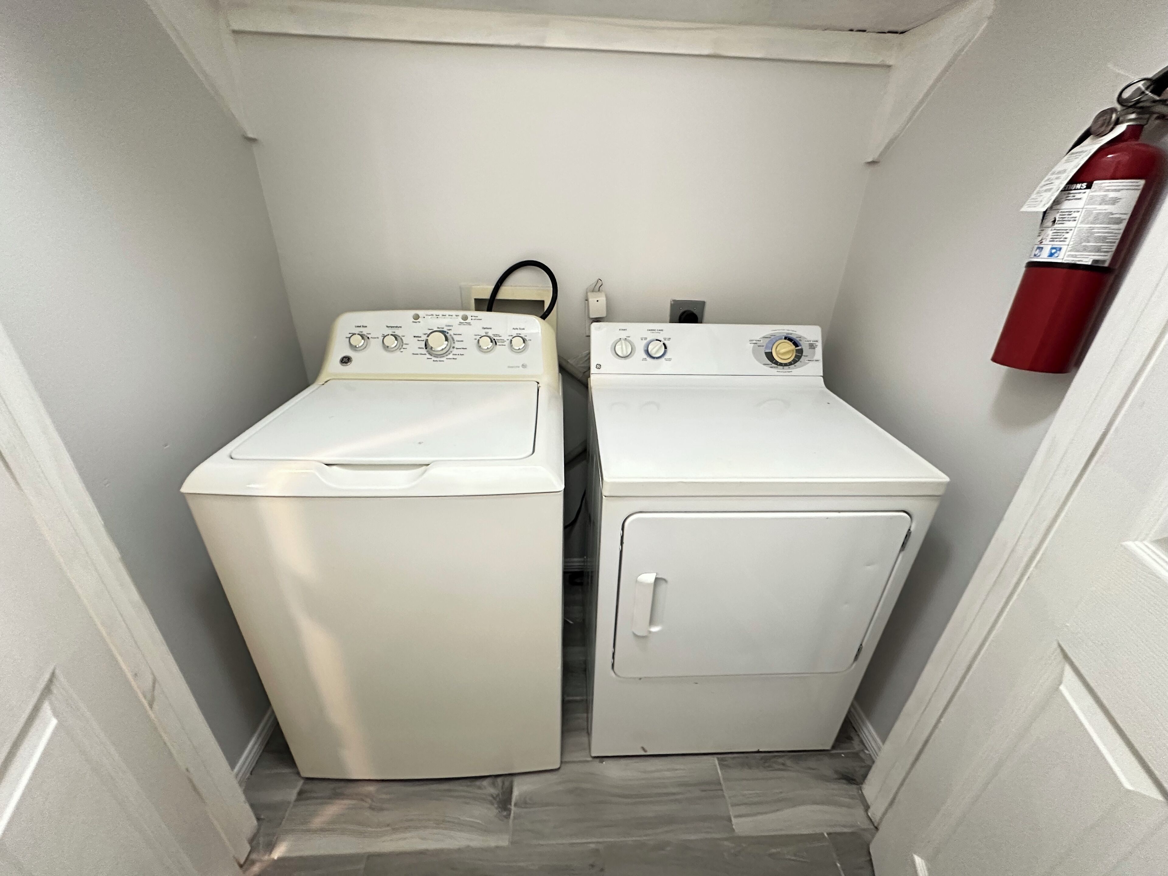 A laundry room with two white washing machines and a red fire extinguisher on the wall.