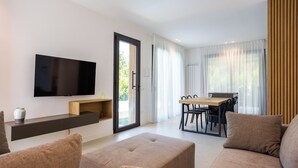 Een moderne woonkamer met een flatscreen-tv, een bank, een voetenbankje en een eethoek met een tafel en stoelen.