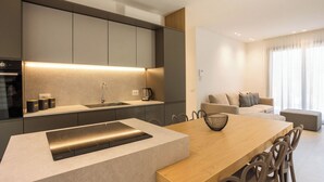 A modern kitchen with a central island, a dining area with a wooden table and chairs, and a living area with a sofa and a coffee table. - Luxury Villa Artemis (Palermo)