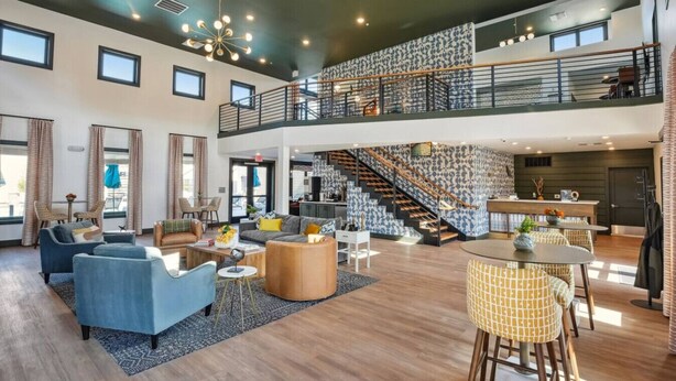 A spacious living area with a high ceiling, a staircase, and a kitchen area.