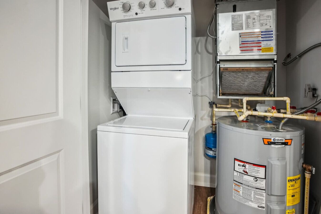 Un cuarto de servicio compacto con lavadora Whirlpool, calentador de agua y medidor de gas.