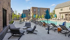 A rooftop pool area with lounge chairs and umbrellas, surrounded by buildings.